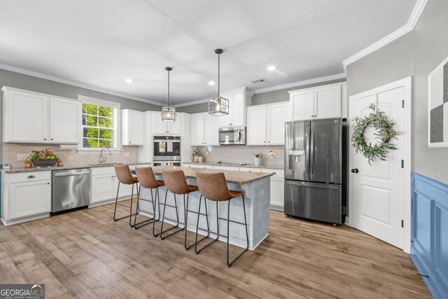 89 Crestview Dr, Guyton, GA 31312 - kitchen with stainless steel appliances, crown molding, a breakfast bar, white cabinetry, and a kitchen island