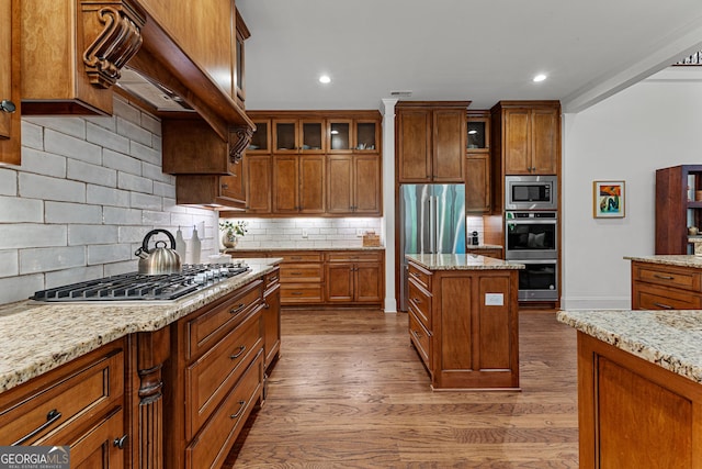 150 Dean Dr, Tyrone, GA 30290 - kitchen featuring stainless steel appliances, brown cabinets, wood finished floors, glass insert cabinets, and decorative backsplash