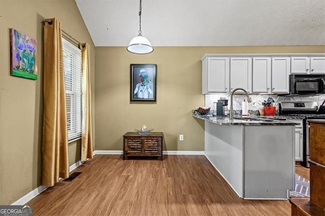 47 Powder Springs St, Hiram, GA 30141 - kitchen featuring black microwave, stainless steel gas range, wood finished floors, vaulted ceiling, and white cabinetry