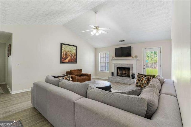 3589 Garden Manor Dr, Loganville, GA 30052 - living room with ceiling fan, wood finished floors, a textured ceiling, a brick fireplace, and lofted ceiling