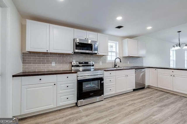 5215 Cordell St, Savannah, GA 31405 - kitchen with appliances with stainless steel finishes, light wood finished floors, dark countertops, white cabinets, and backsplash