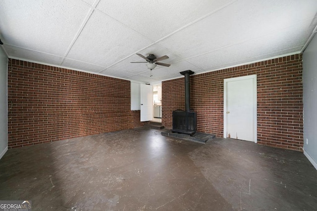 213 Cook St, Cartersville, GA 30120 - unfurnished living room with a wood stove, ceiling fan, brick wall, a paneled ceiling, and concrete floors