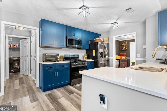3229 Dunlin Lake Rd, Lawrenceville, GA 30044 - kitchen featuring stainless steel appliances, washer / clothes dryer, blue cabinetry, light countertops, and light wood-type flooring