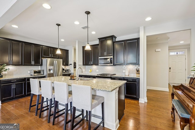8215 Harlond Way, Suwanee, GA 30024 - kitchen featuring stainless steel appliances, backsplash, a breakfast bar, light stone counters, and a kitchen island with sink