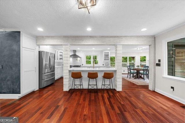 4735 Log Cabin Rd, Gainesville, GA 30504 - kitchen featuring stainless steel refrigerator with ice dispenser, decorative columns, wall chimney range hood, a breakfast bar area, and dark wood-style floors