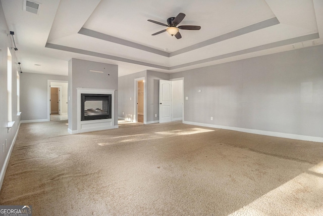 7691 Brazos Trl, Fairburn, GA 30213 - unfurnished living room featuring a raised ceiling, a ceiling fan, carpet flooring, and a multi sided fireplace