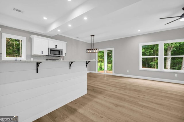 155 Carey St, Franklin Springs, GA 30662 - kitchen with stainless steel microwave, a breakfast bar, ceiling fan, white cabinetry, and light wood-style floors