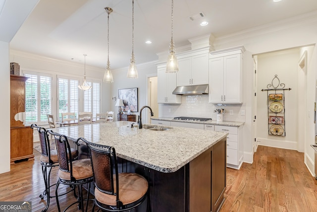 1911 Bent Pine Park, Statham, GA 30666 - kitchen with under cabinet range hood, an island with sink, light wood-style flooring, a breakfast bar area, and ornamental molding