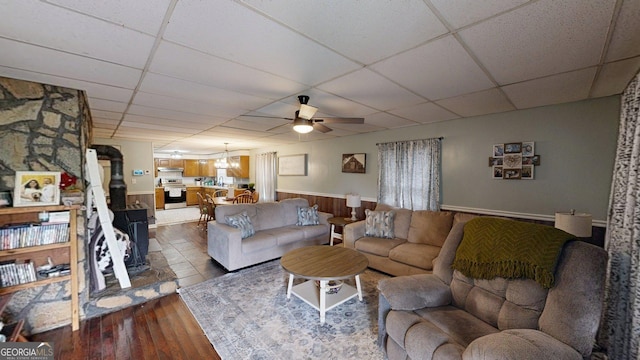 15 Aragon Rd, Aragon, GA 30104 - living room featuring a drop ceiling, a wood stove, a ceiling fan, dark wood-style flooring, and wainscoting