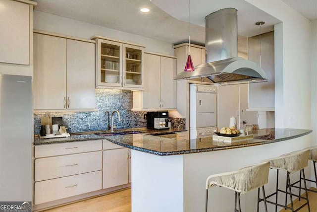 2575 Peachtree Rd NE Unit 15G, Atlanta, GA 30305 - kitchen with island exhaust hood, a breakfast bar, dark stone counters, decorative backsplash, and washer / clothes dryer