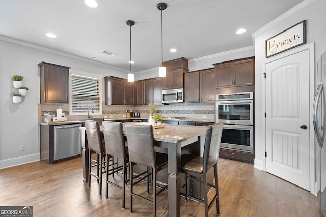 2767 NW Magnolia Creek Dr, Kennesaw, GA 30152 - kitchen featuring appliances with stainless steel finishes, dark brown cabinets, a breakfast bar area, decorative backsplash, and a center island
