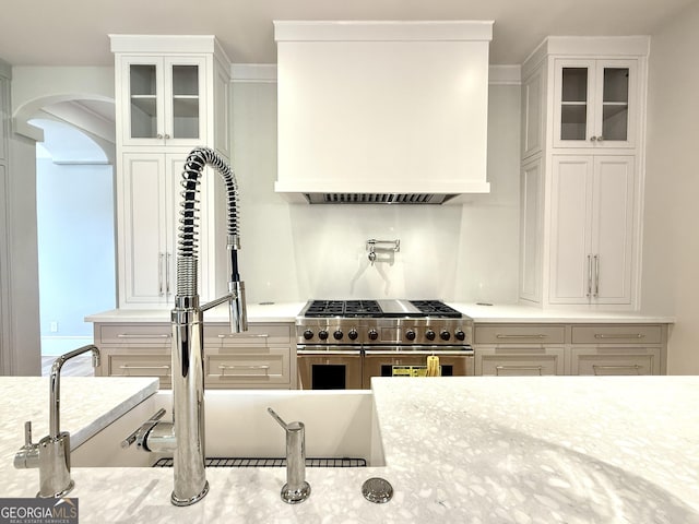 1005 Haddie Way, Alpharetta, GA 30004 - kitchen with double oven range, arched walkways, glass insert cabinets, custom range hood, and white cabinetry