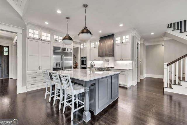 481 Meadow Lake Ter, Hoschton, GA 30548 - kitchen featuring appliances with stainless steel finishes, custom exhaust hood, ornamental molding, dark wood-style floors, and a kitchen island with sink