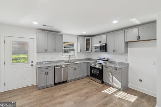 4179 Hanes Dr, Decatur, GA 30035 - kitchen with stainless steel appliances, gray cabinetry, glass insert cabinets, light stone counters, and light wood finished floors