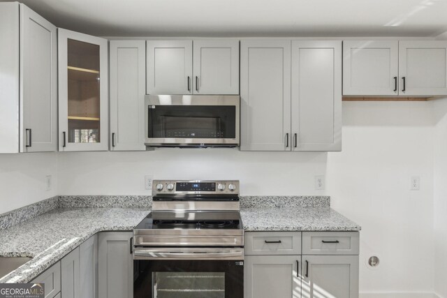 4179 Hanes Dr, Decatur, GA 30035 - kitchen featuring stainless steel appliances, glass insert cabinets, light stone counters, and gray cabinets