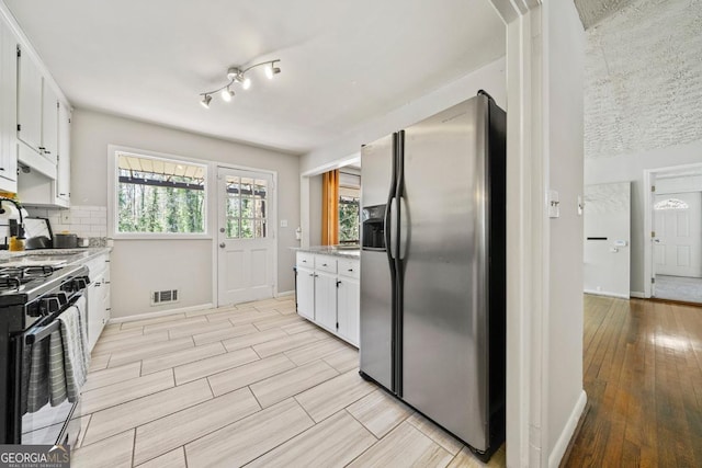 1755 Fairburn Rd SW, Atlanta, GA 30331 - kitchen with stainless steel fridge, range with gas stovetop, light wood-style floors, white cabinets, and decorative backsplash