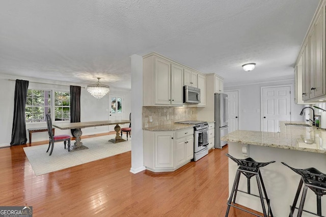 2095 Honeysuckle Dr, Cumming, GA 30040 - kitchen with appliances with stainless steel finishes, a kitchen bar, a chandelier, backsplash, and light wood-type flooring