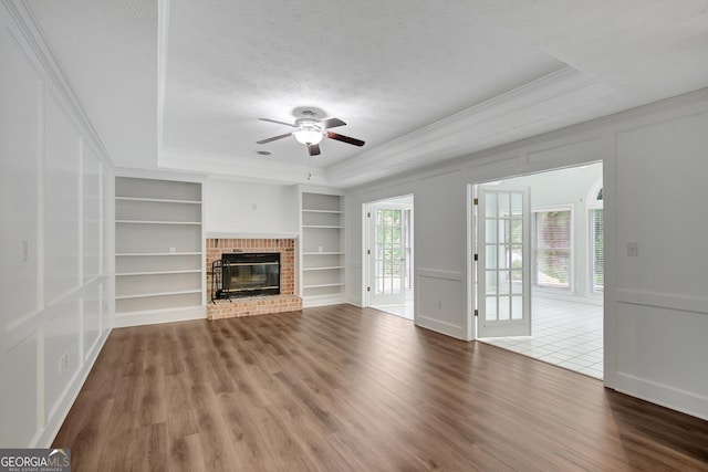 40 Springwater Chase, Newnan, GA 30265 - unfurnished living room featuring built in shelves, crown molding, a ceiling fan, wood finished floors, and a tray ceiling