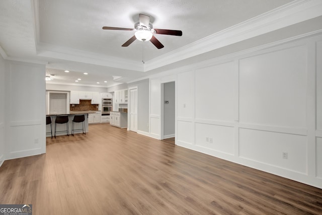 40 Springwater Chase, Newnan, GA 30265 - unfurnished living room with a ceiling fan, a tray ceiling, ornamental molding, a decorative wall, and wood finished floors