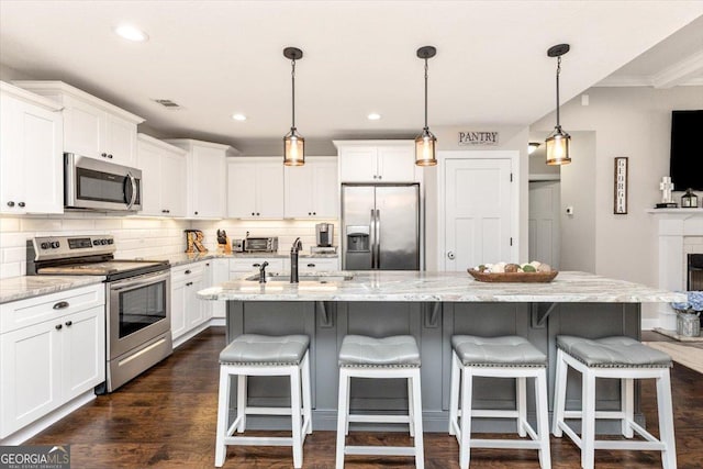 311 Kendall Ct, Perry, GA 31069 - kitchen with stainless steel appliances, white cabinetry, tasteful backsplash, a center island with sink, and light stone counters