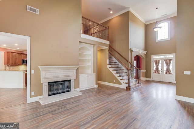 3217 Aberrone Pl, Buford, GA 30519 - unfurnished living room featuring a high ceiling, stairway, a glass covered fireplace, wood finished floors, and crown molding
