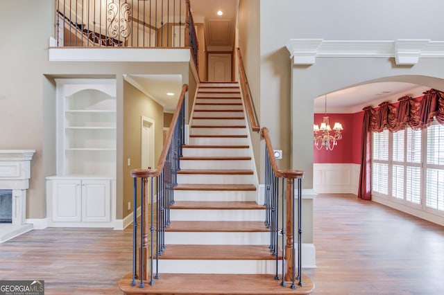 3217 Aberrone Pl, Buford, GA 30519 - staircase featuring wood finished floors, a chandelier, a towering ceiling, crown molding, and a glass covered fireplace