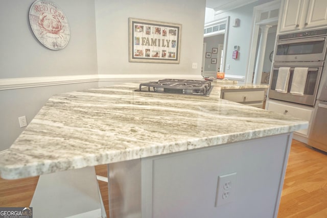 361 Fairway Cir, Monroe, GA 30656 - kitchen featuring appliances with stainless steel finishes, light wood-style flooring, light stone countertops, ornamental molding, and a center island