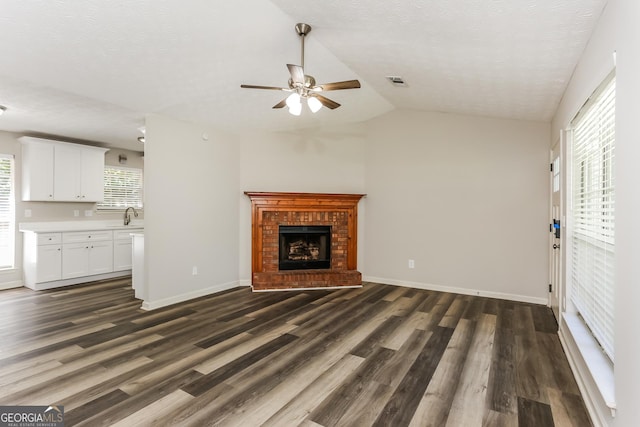1421 Oak Knoll Dr NE, Conyers, GA 30012 - unfurnished living room featuring a ceiling fan, dark wood-style flooring, a brick fireplace, lofted ceiling, and a textured ceiling