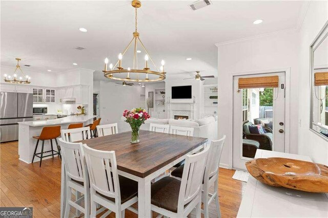 162 Drakes Lndg, Brunswick, GA 31523 - dining area featuring a chandelier, a warm lit fireplace, ceiling fan, light wood-style floors, and recessed lighting
