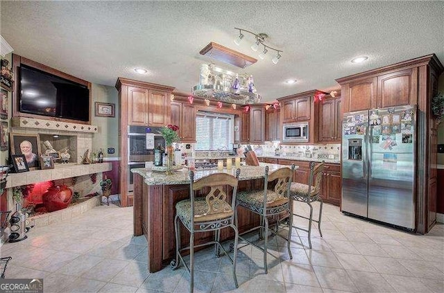 186 Wolverine Dr, Waleska, GA 30183 - kitchen featuring appliances with stainless steel finishes, light tile patterned floors, a textured ceiling, backsplash, and a breakfast bar