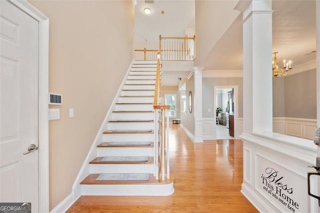 1979 Spivey Vlg, Jonesboro, GA 30236 - stairs featuring crown molding, ornate columns, wood finished floors, a wainscoted wall, and a chandelier