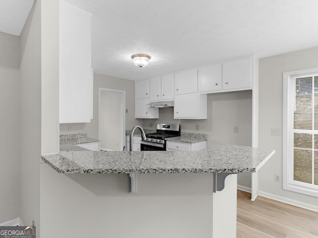 404 Northwind Pl, Stockbridge, GA 30281 - kitchen featuring stainless steel gas range, under cabinet range hood, a peninsula, light wood-type flooring, and white cabinets