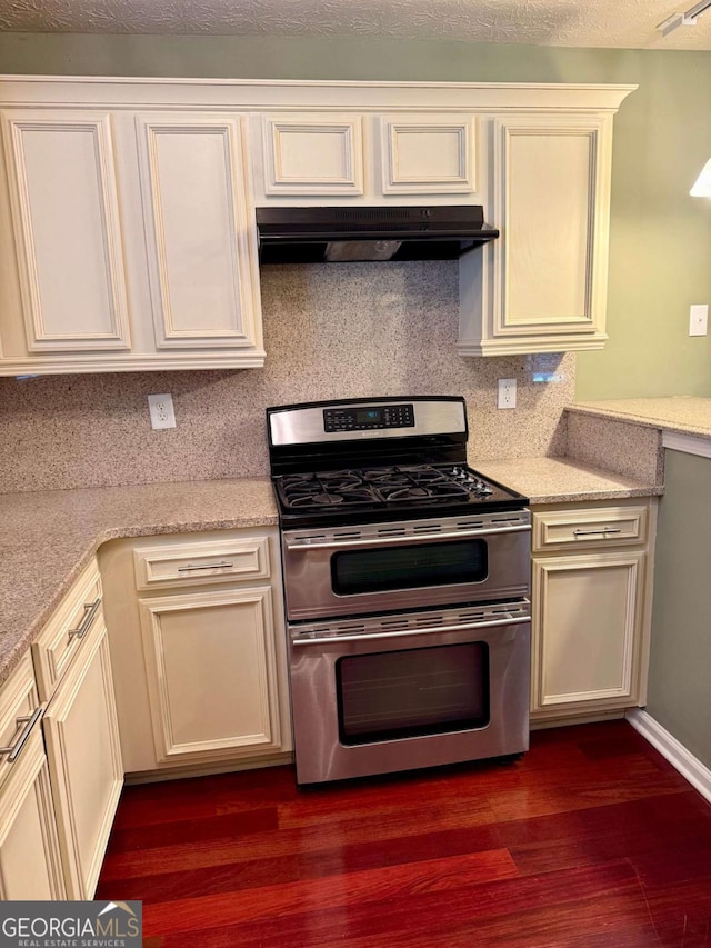 1013 Navaho Trl, Monroe, GA 30655 - kitchen featuring range with two ovens, under cabinet range hood, dark wood-style flooring, decorative backsplash, and cream cabinetry