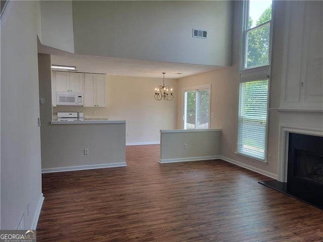 13565 Weycroft Cir, Alpharetta, GA 30004 - unfurnished living room with a chandelier, dark wood-style floors, a fireplace with raised hearth, and a towering ceiling