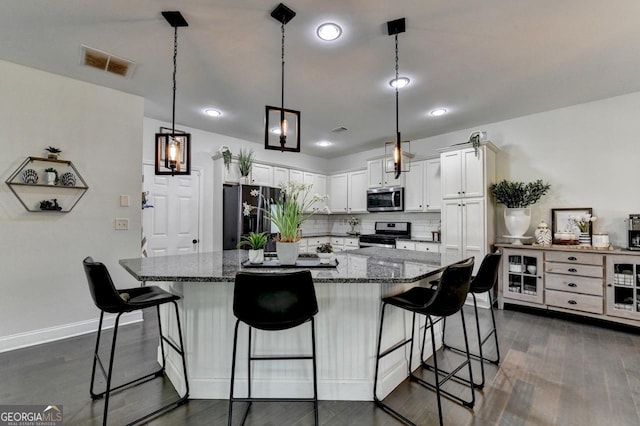 2410 Melton Common Dr, Dacula, GA 30019 - kitchen featuring stainless steel appliances, white cabinets, dark wood-style flooring, a kitchen bar, and dark stone countertops