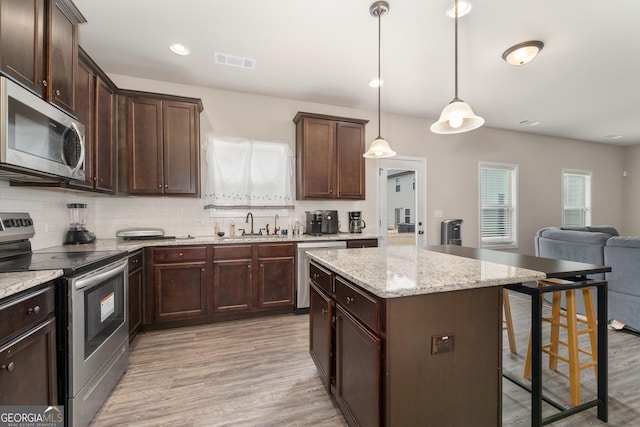 2277 Church St, Hampton, GA 30228 - kitchen featuring appliances with stainless steel finishes, a breakfast bar, light wood-type flooring, backsplash, and dark brown cabinetry