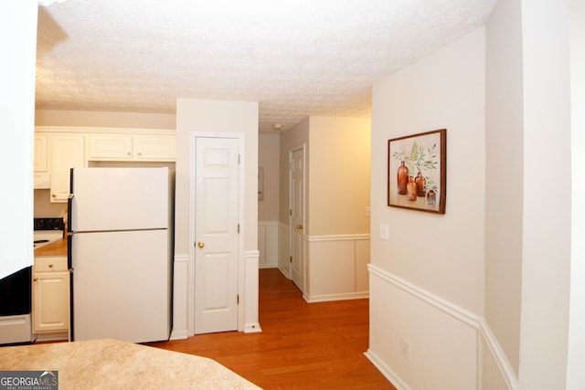 555 Flintlock Dr, Dacula, GA 30019 - kitchen with freestanding refrigerator, light wood-type flooring, a textured ceiling, light countertops, and a wainscoted wall