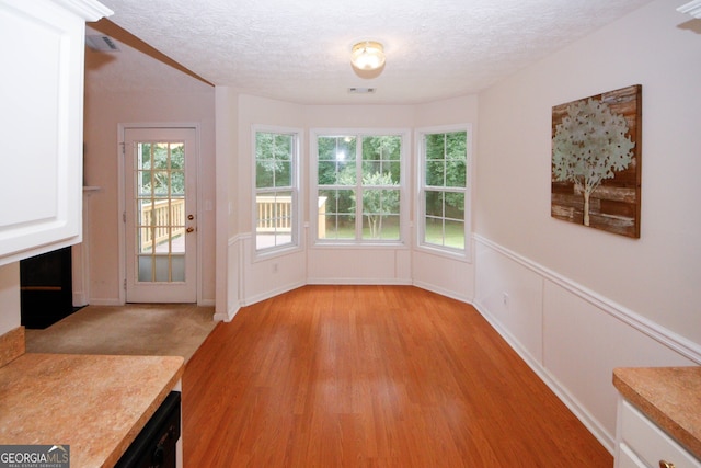 555 Flintlock Dr, Dacula, GA 30019 - unfurnished dining area with light wood-style floors, a textured ceiling, and wainscoting