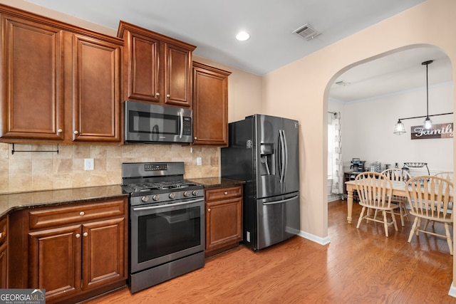 305 Hidden Creek Ln, Canton, GA 30114 - kitchen featuring appliances with stainless steel finishes, arched walkways, light wood-style floors, tasteful backsplash, and dark stone countertops