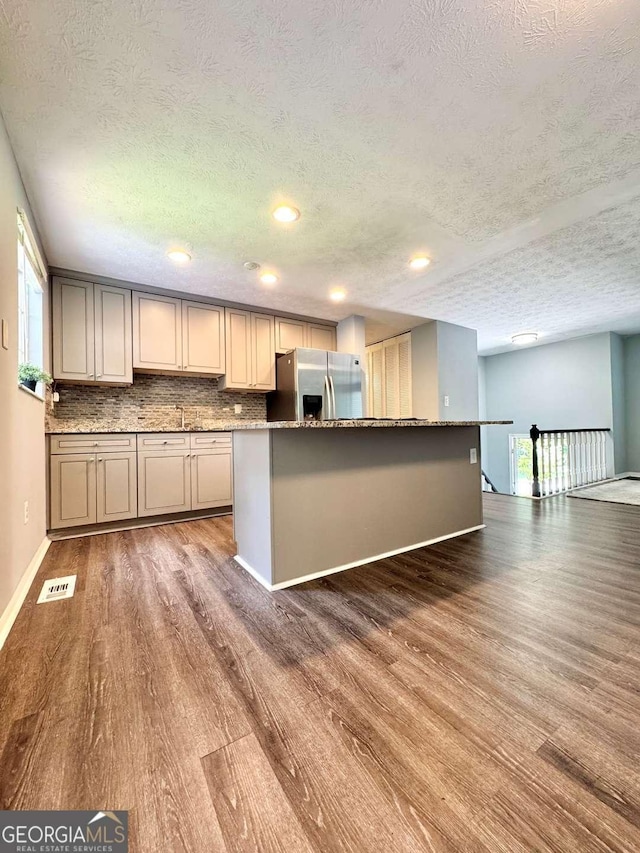 3544 Citrus Dr, Duluth, GA 30096 - kitchen featuring stainless steel fridge, a textured ceiling, wood finished floors, decorative backsplash, and dark stone countertops