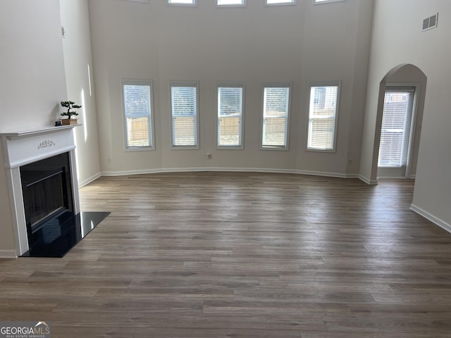 1238 Polk Xing, Mcdonough, GA 30252 - unfurnished living room featuring a fireplace, arched walkways, a towering ceiling, and wood finished floors