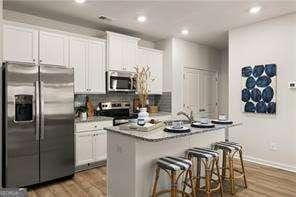 42 Buckingham Ln Unit 233, Hoschton, GA 30548 - kitchen with appliances with stainless steel finishes, wood finished floors, a kitchen breakfast bar, white cabinetry, and an island with sink