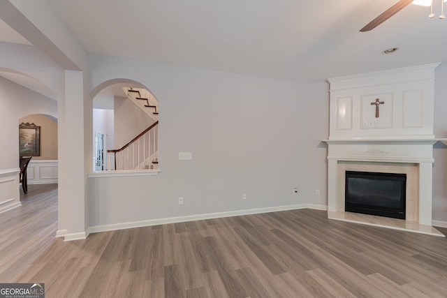 2940 Bentbill Xing, Cumming, GA 30041 - unfurnished living room with light wood-style flooring, ceiling fan, a premium fireplace, stairs, and arched walkways