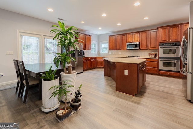 2940 Bentbill Xing, Cumming, GA 30041 - kitchen featuring stainless steel appliances, a kitchen island, tasteful backsplash, light countertops, and light wood-type flooring