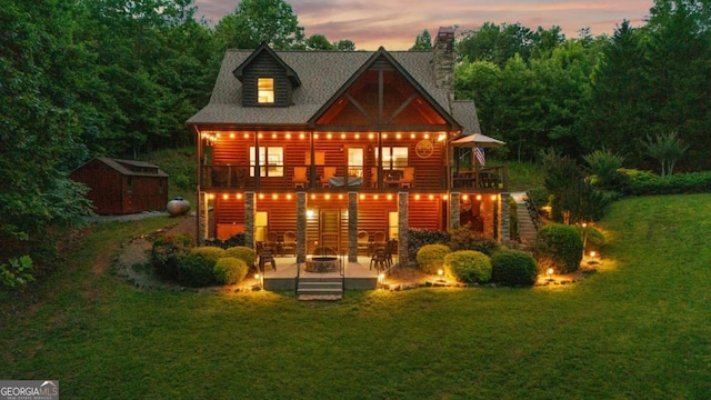 2357 Haven Heights Rd, Hiawassee, GA 30546 - back of house at dusk featuring a patio, a yard, a shed, faux log siding, and a chimney