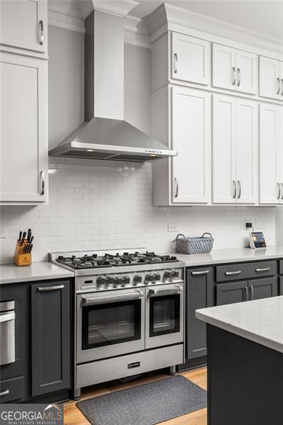 127 Oak Ln, Decatur, GA 30030 - kitchen with wall chimney exhaust hood, stainless steel gas range oven, light countertops, light wood-style floors, and gray cabinets