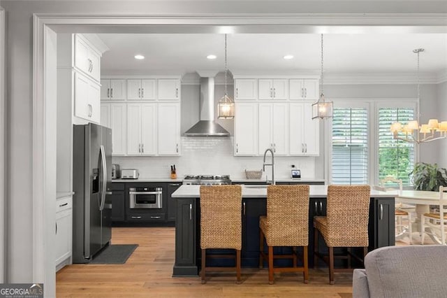 127 Oak Ln, Decatur, GA 30030 - kitchen featuring wall chimney exhaust hood, appliances with stainless steel finishes, light countertops, a chandelier, and white cabinetry