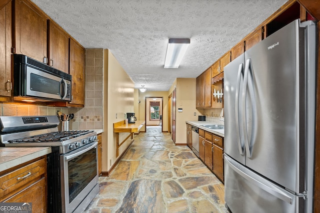 1290 Shadowlawn Dr NE, Conyers, GA 30012 - kitchen with appliances with stainless steel finishes, stone floors, brown cabinetry, tasteful backsplash, and a textured ceiling