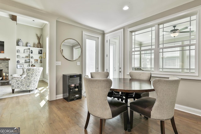 459 N Cove Dr, Newnan, GA 30263 - dining area with beverage cooler, crown molding, a stone fireplace, a ceiling fan, and wood finished floors