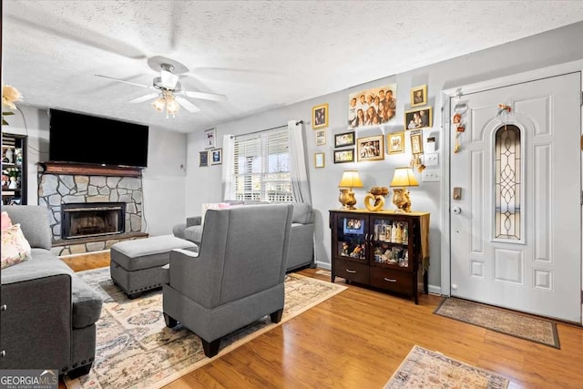 916 Marshall Fuller Rd, Dallas, GA 30157 - living area featuring wood finished floors, a ceiling fan, a textured ceiling, and a stone fireplace